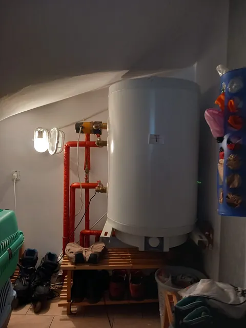 Stojący zasobnik ciepłej wody podłączony do instalacji w pomieszczeniu technicznym